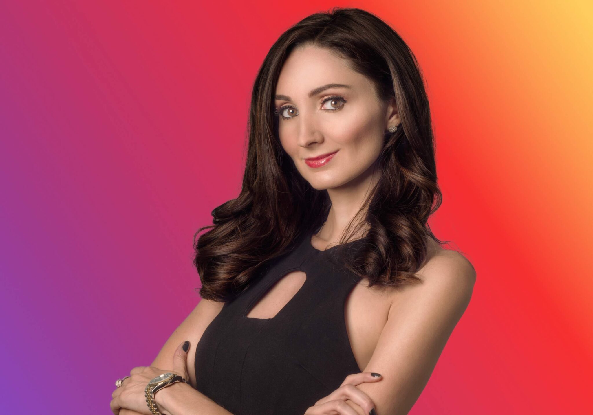 Google SEO Expert Kristen Ruby CEO of Ruby Media Group Image. A brunette woman named Kris Ruby, a social media marketing expert, with long brown hair wearing a black dress poses with folded arms in front of a gradient background.